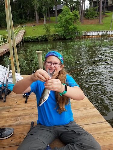 A Troop 19 member smiles and holds up a small fish that she was caught.